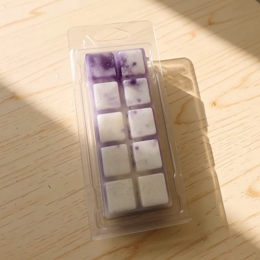 Clamshell med lilla og hvit duftvoks/smeltevoks med duft av sitrus og pepper, milde blomster, vanilje og musk